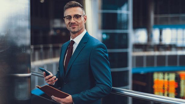 Confident businessman in a suit holding a phone and notebook.