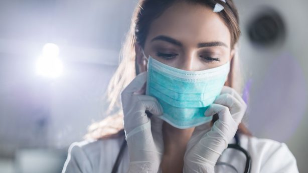 Female doctor adjusting her surgical mask in a medical setting.